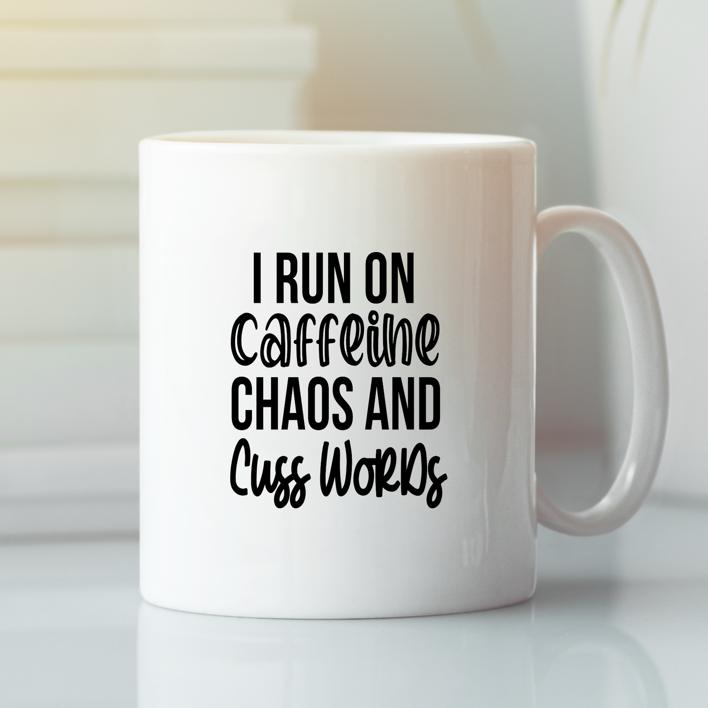 The Caffeine Chaos Cuss Words Mug | Funny Coffee Gift features bold black text and a glossy finish, adding a sarcastic twist to your daily routine as it sits stylishly on any surface against a blurred background.