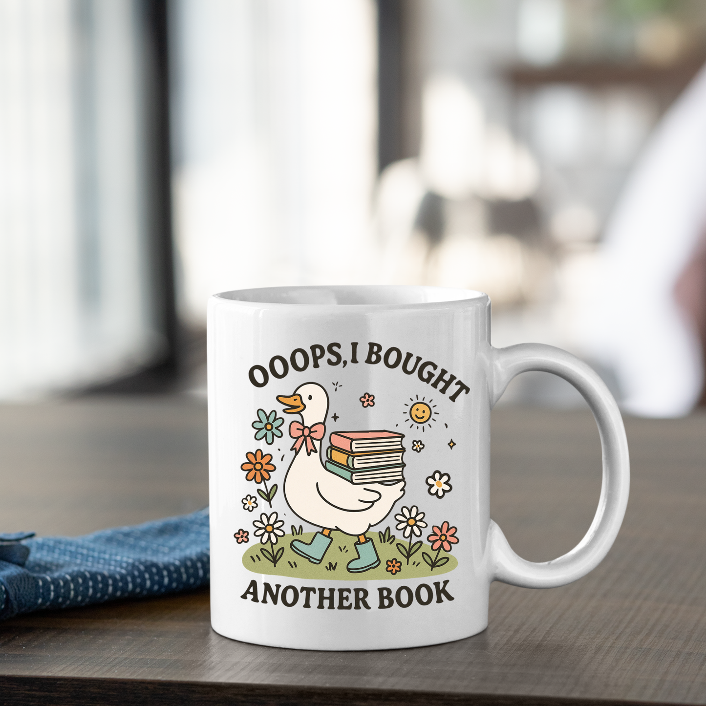 The Book Lover Mug | Ooops, I Bought Another Book Goose features a cute goose holding books and surrounded by flowers with playful text. A perfect cottagecore gift for any book lover! Blue napkin not included.