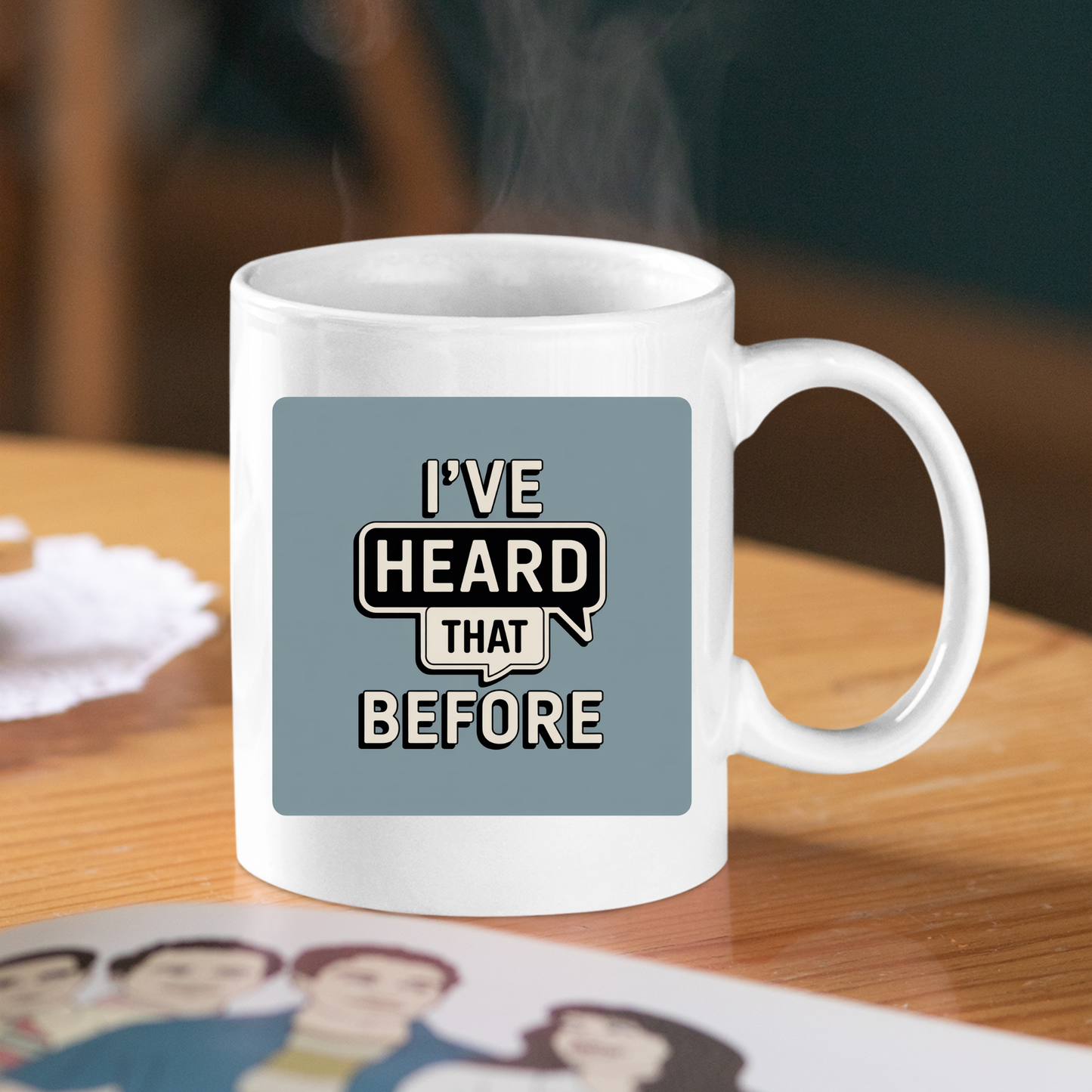 The "I've Heard That Before Mug | Office Humor Coffee Cup" is a white ceramic mug featuring the phrase “I’ve heard that before” printed boldly—an ideal choice for those who enjoy a touch of sarcasm at work. Perfect as a funny office mug, it is shown resting on a wooden table beside a coaster and a partially visible illustrated item.