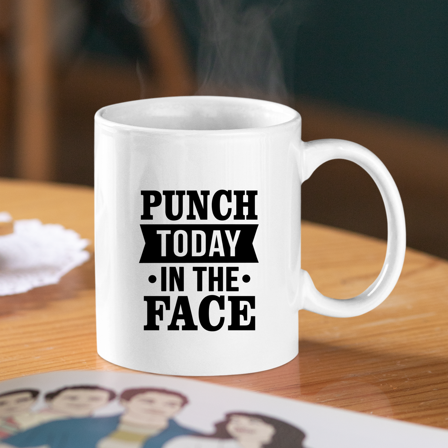 The Punch Today in the Face Mug | Bold Motivational Coffee Cup sits on a wooden table, steam rising as its striking black text inspires you—perfect for energizing your morning routine. A blurred illustration appears in the foreground.