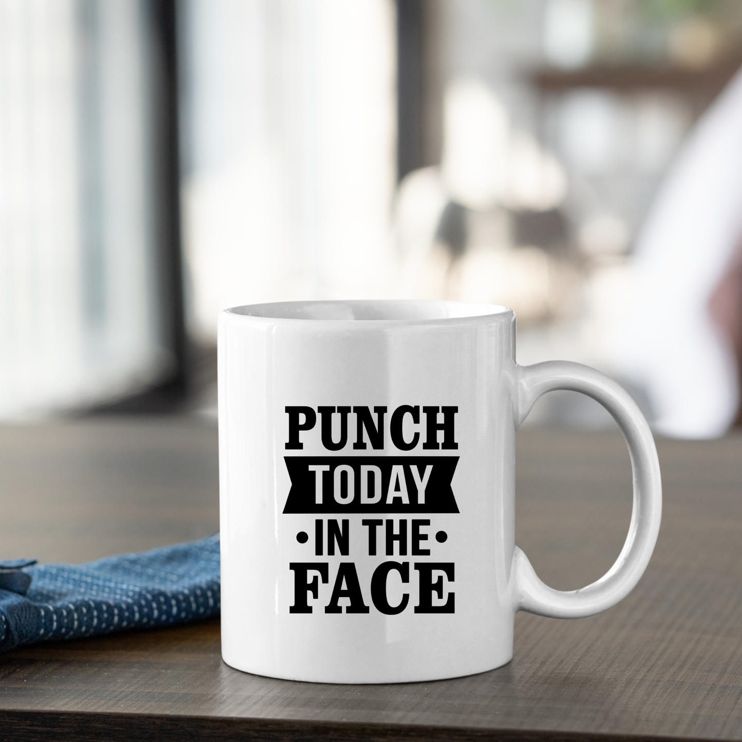 The Punch Today in the Face Mug | Bold Motivational Coffee Cup sits on a wooden table with eye-catching text, paired with a blue cloth napkin—perfect as a funny gift or motivational mug in any setting.