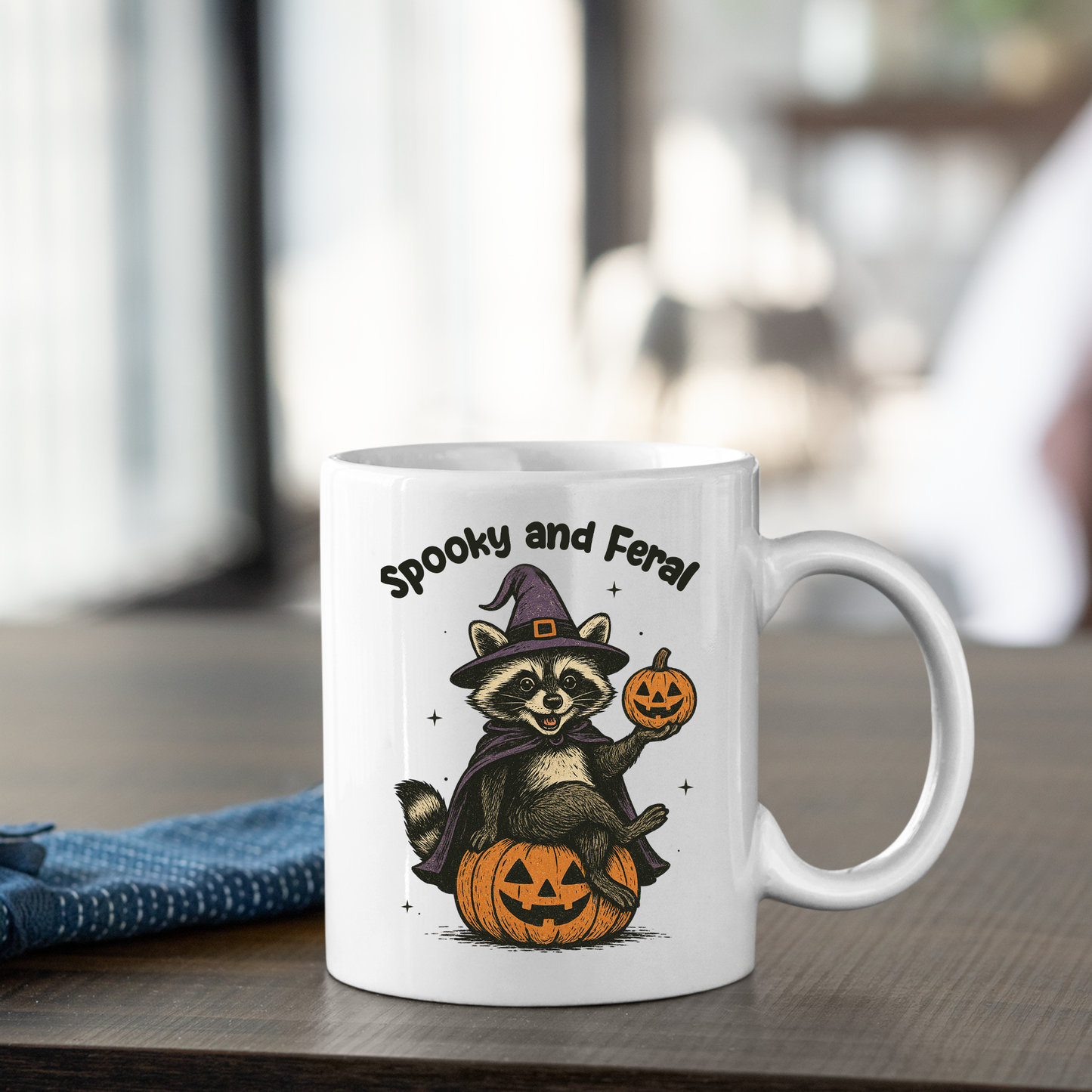 The "Spooky and Feral Raccoon Mug | Funny Halloween Gift" features a raccoon in a purple witch hat, holding a pumpkin on a jack-o'-lantern with "Spooky and Feral" above—a perfect Halloween mug for raccoon lovers!.