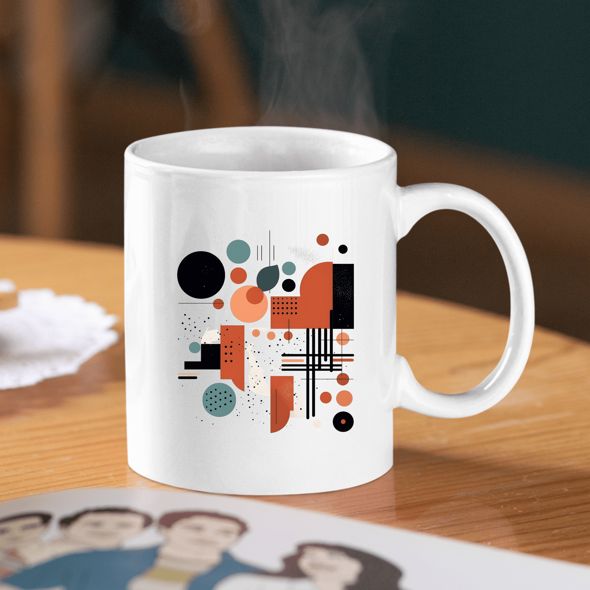The Atomic Sunrise Mid Century Modern Mug, featuring a white base and an abstract geometric design in black, orange, and teal, sits on a wooden table with rising steam. A partial photo of three people appears in the foreground.