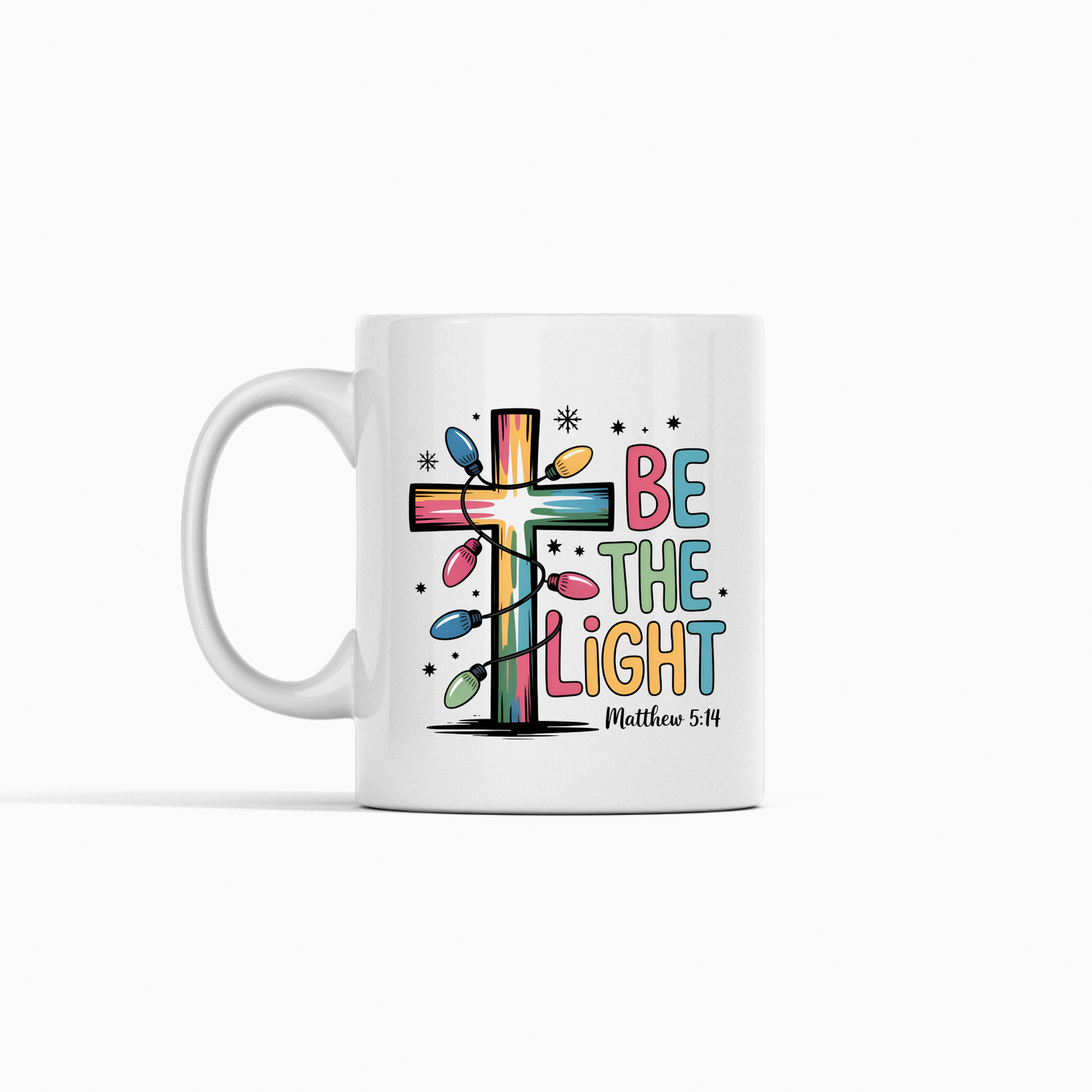 The Be the Light Matthew 5:14 Christmas Mug is a white coffee mug with a colorful cross wrapped in Christmas lights and "Be the Light Matthew 5:14" in playful, multicolored letters—perfect to inspire faith daily.