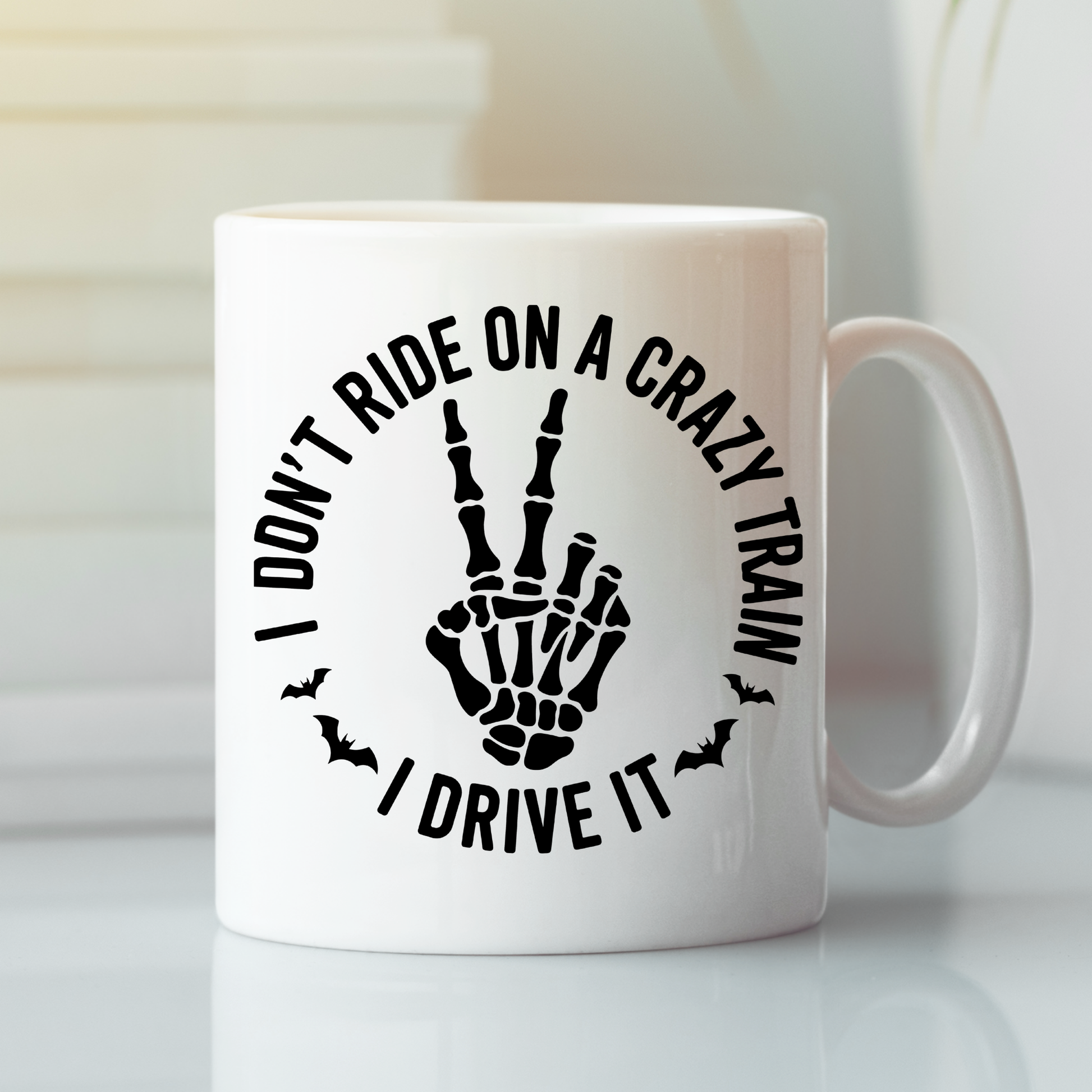 The Crazy Train Mug | Chaos Coffee Cup for Daily Mayhem showcases bold black text that declares, "I DON'T RIDE ON A CRAZY TRAIN, I DRIVE IT," circling a skeleton hand giving a peace sign with two small bat accents. Ideal for anyone who enjoys their coffee with attitude and dark humor, this mug is perfect as a sarcastic or edgy gift.