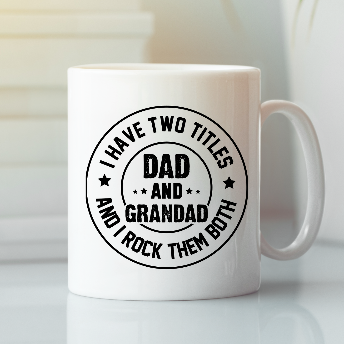The Dad and Grandad Mug | Gift for Proud Grandad is a white ceramic coffee mug featuring black text that reads, "I have two titles Dad and Grandad and I rock them both." Placed on a white surface with a blurred background, this thoughtful mug makes an ideal Father's Day gift.