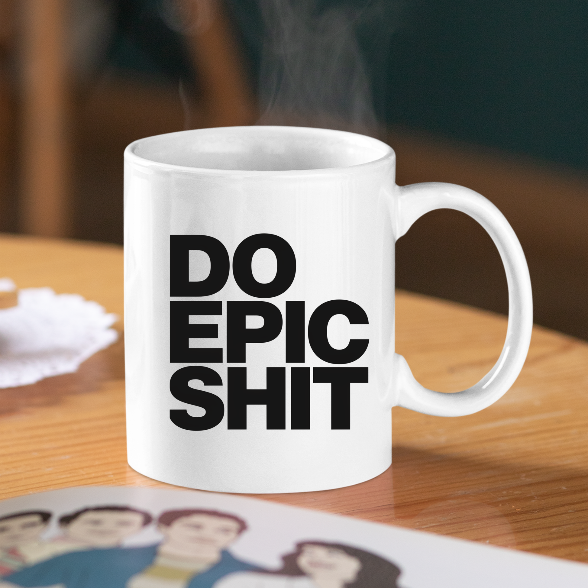 A white Do Epic Shit Mug | Funny Motivational Coffee Mug sits on a wooden table, emblazoned with the bold black message "DO EPIC SHIT." Steam curls invitingly from the cup, while part of a photo featuring illustrated people is visible in the foreground—making this mug an ideal gift for entrepreneurs who appreciate both humor and inspiration.