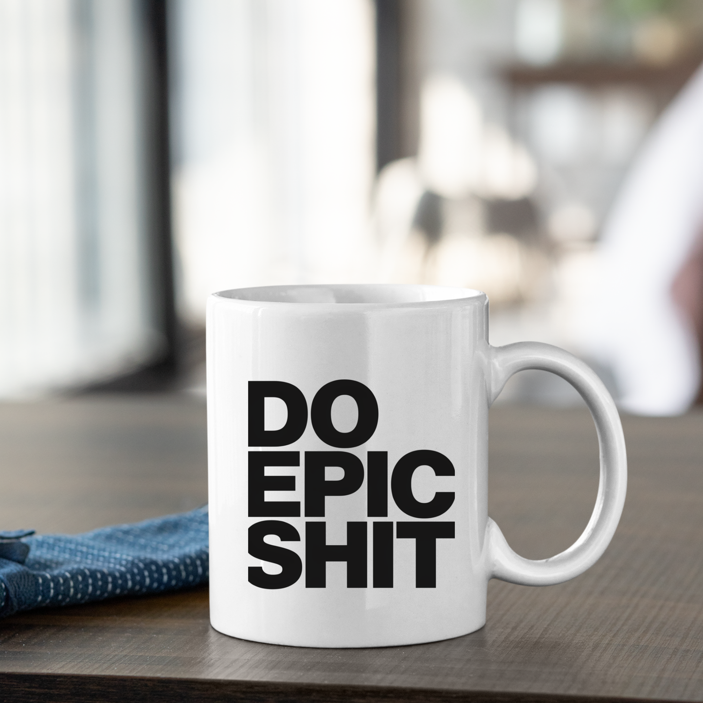 A Do Epic Shit Mug | Funny Motivational Coffee Mug sits on a table, featuring bold black lettering that reads “DO EPIC SHIT” against a crisp white background. A folded blue cloth rests beside the mug, and the softly blurred background highlights its appeal—making this an ideal gift for entrepreneurs who love starting their day with a dose of motivation.