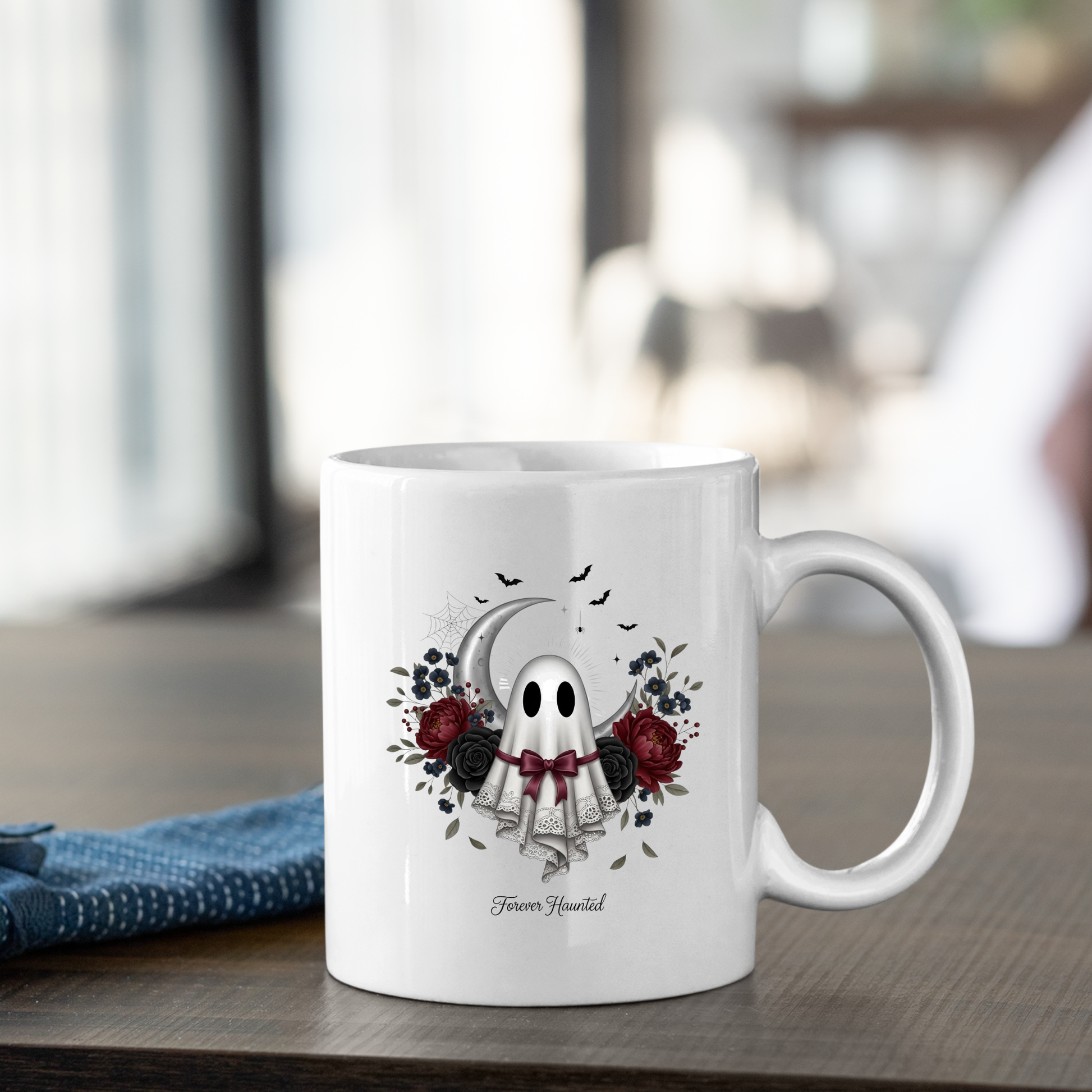 The Forever Haunted Ghost Mug | Gothic Halloween Coffee Mug sits on a wooden table, adorned with a cute ghost, tarot cards, dark roses, a crescent moon, and small bats. Below the enchanting design is the phrase “Favor Yourself,” making this mug the perfect choice for your Halloween coffee rituals. A blue napkin rests beside it.