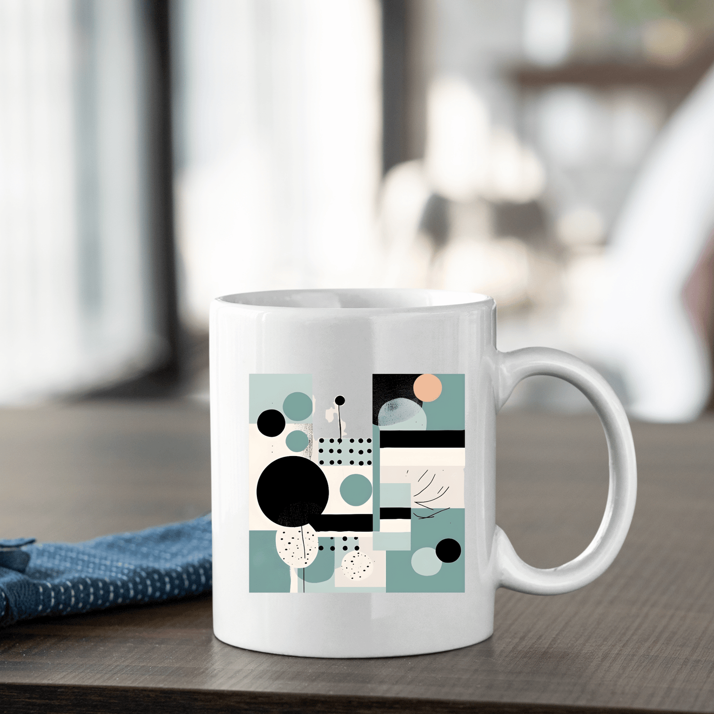The Harbor Morning Mid Century Modern Mug, crafted in white ceramic with black, teal, peach, and beige geometric accents, rests on a wooden table near a blue cloth—an ideal spring decor piece for cozy indoor spaces.