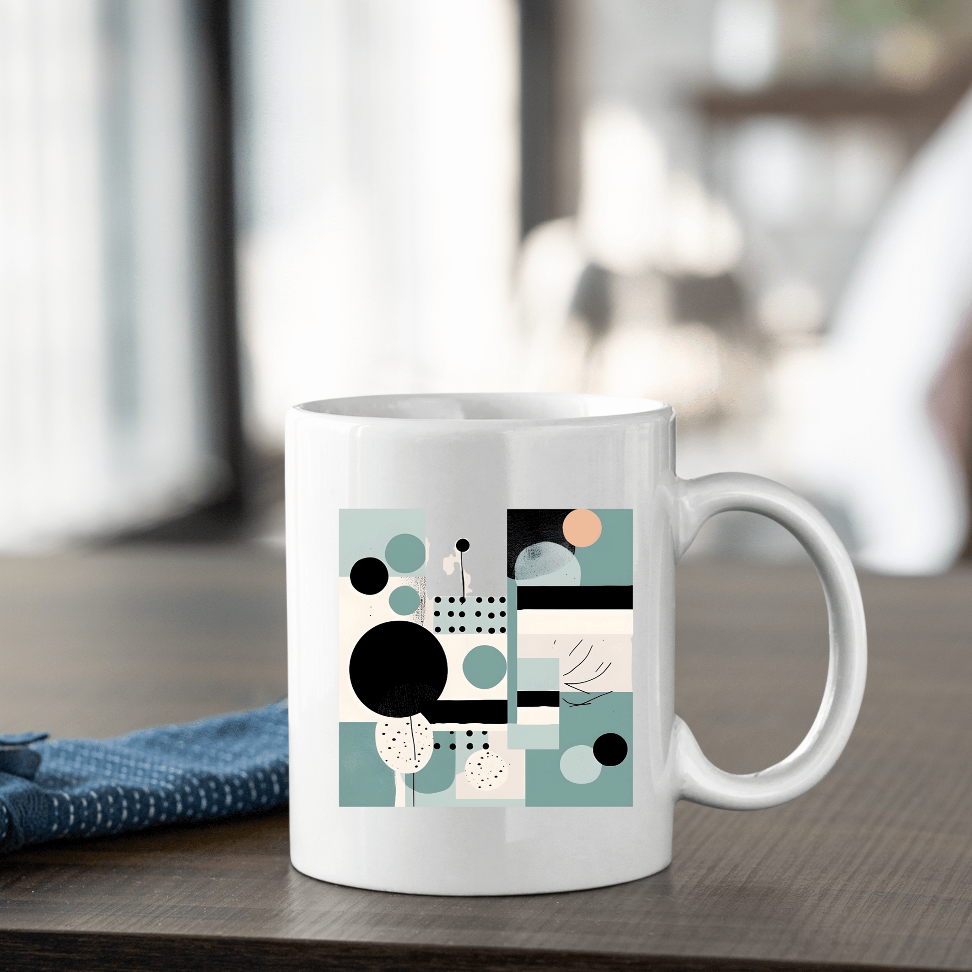 The Harbor Morning Mid Century Modern Mug, crafted in white ceramic with black, teal, peach, and beige geometric accents, rests on a wooden table near a blue cloth—an ideal spring decor piece for cozy indoor spaces.