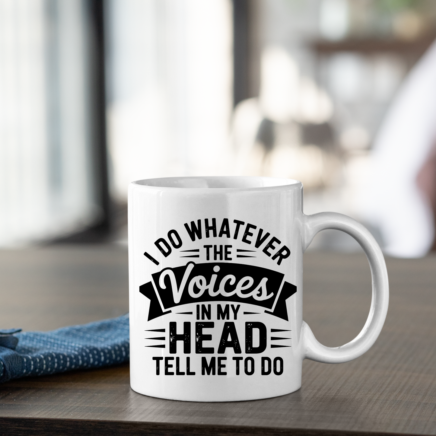 The Voices in My Head Mug | Sarcastic Coffee Gift sits on a table, featuring the witty text: "I do whatever the voices in my head tell me to do." This playful white coffee mug is perfect for anyone who loves to start their day with a dose of humor.