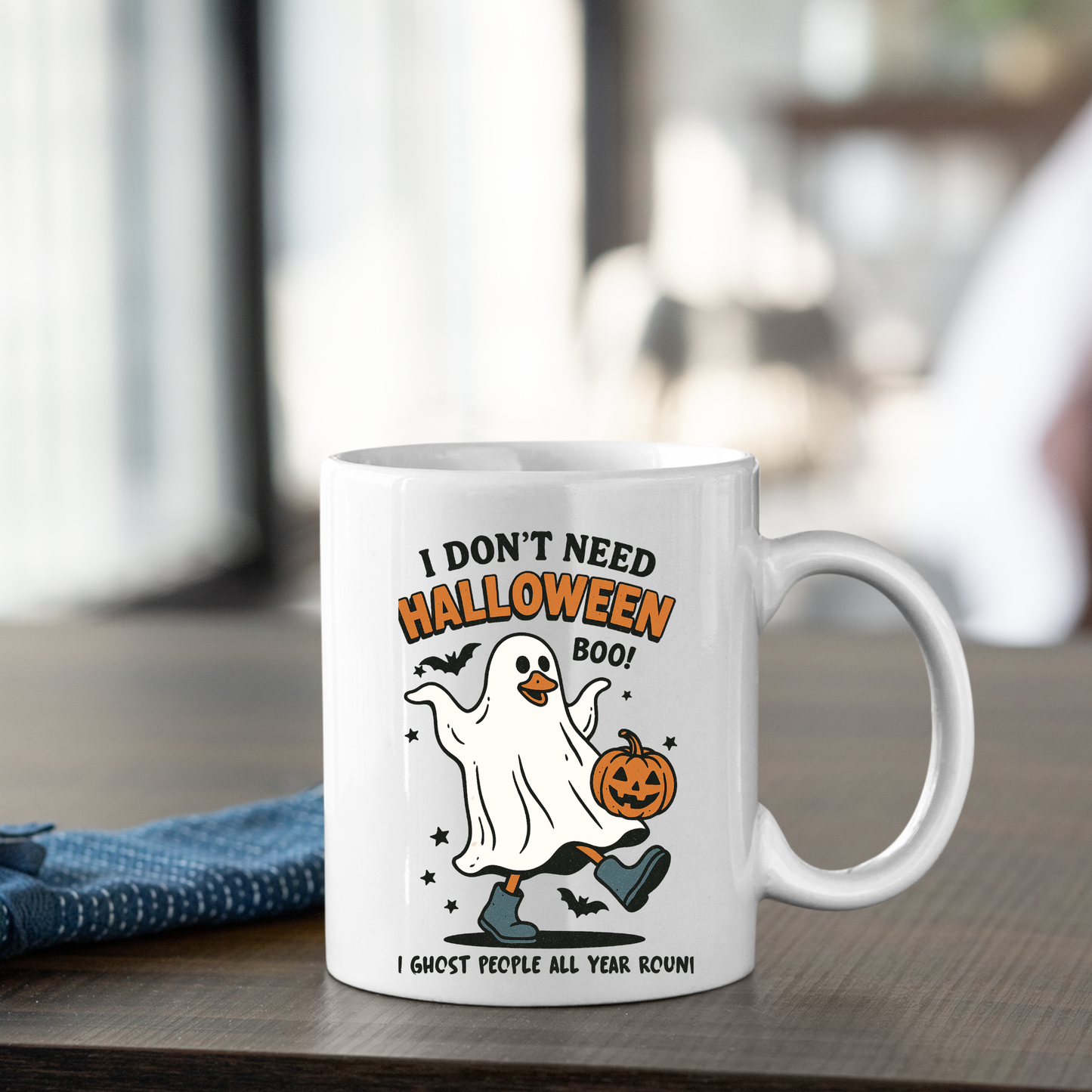 The Funny Ghost Mug | I Don’t Need Halloween Boo Cup features a white design with a cartoon ghost holding a jack-o’-lantern, surrounded by bats and the text: “I DON’T NEED HALLOWEEN BOO! I ghost people all year round.”.