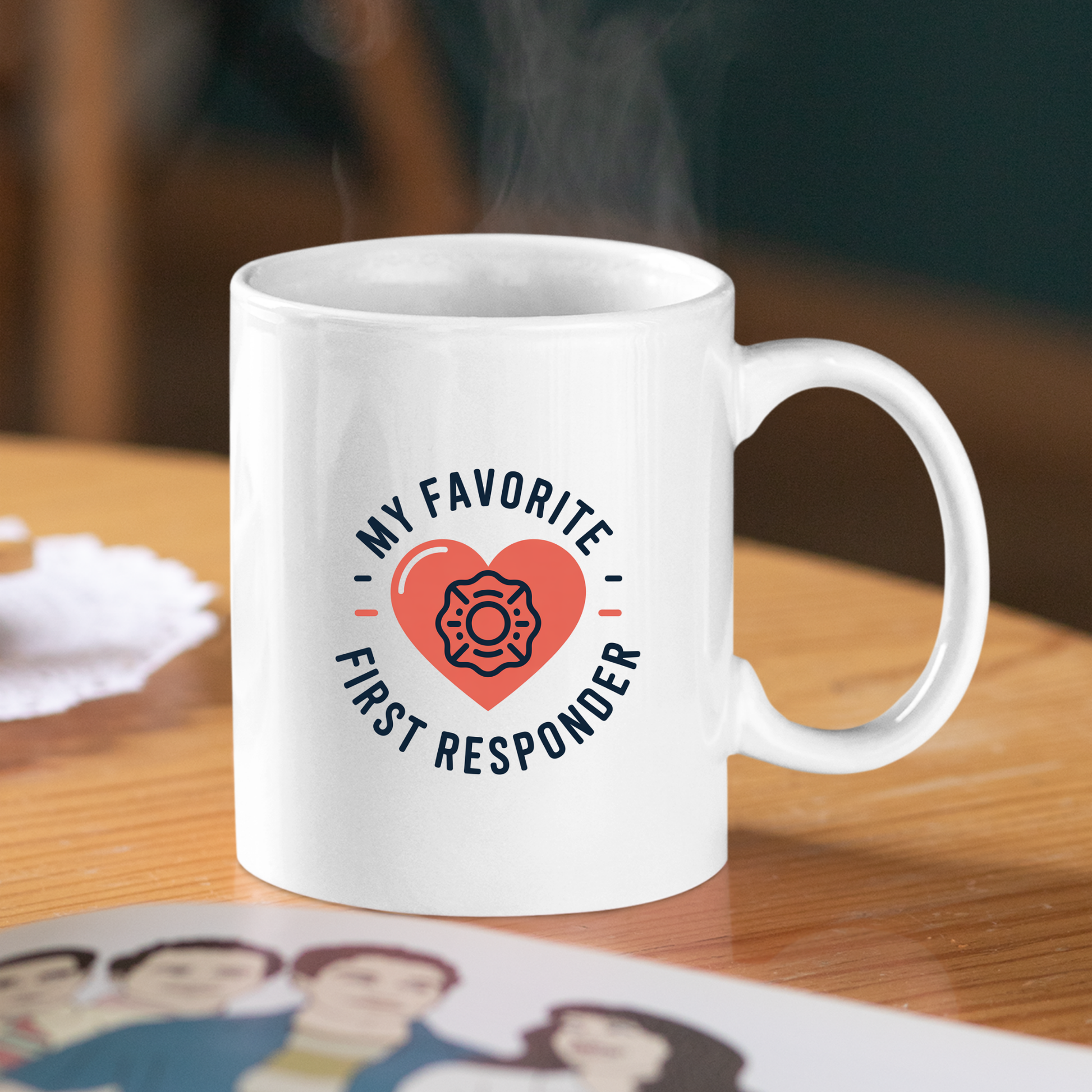 The "My Favorite First Responder Mug | Appreciation Gift" is a white mug featuring a red heart and firefighter symbol with the phrase "My favorite first responder." The mug sits on a wooden table beside a sketch of four people, with steam gently rising from it—a heartfelt gift idea for first responders.