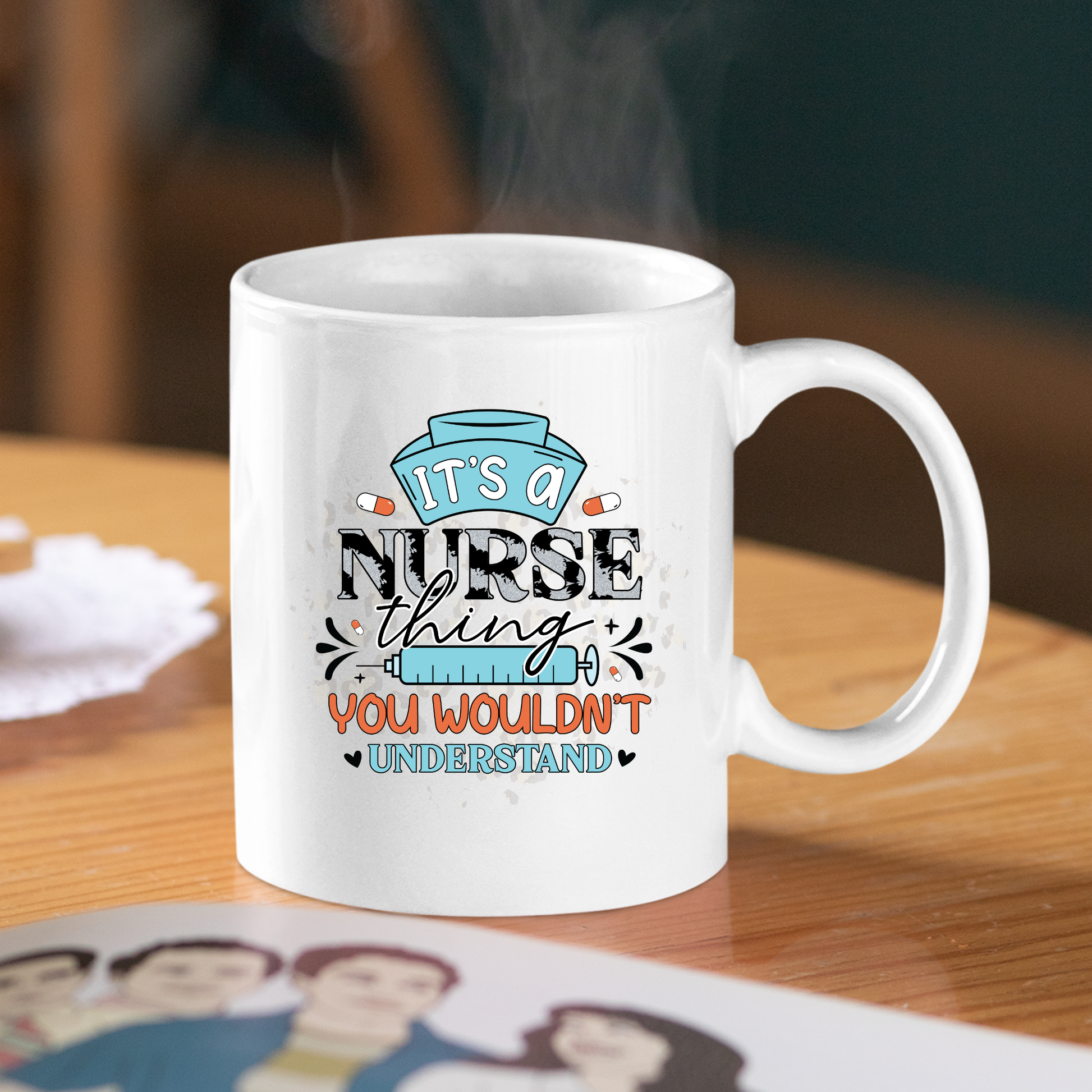 The Funny Nurse Mug Gift | It's a Nurse Thing Design features a white mug with "It's a nurse thing, you wouldn't understand" and nurse cap and syringe artwork—an ideal gift for any healthcare hero. Placed on a table beside a magazine, steam rises from the mug.