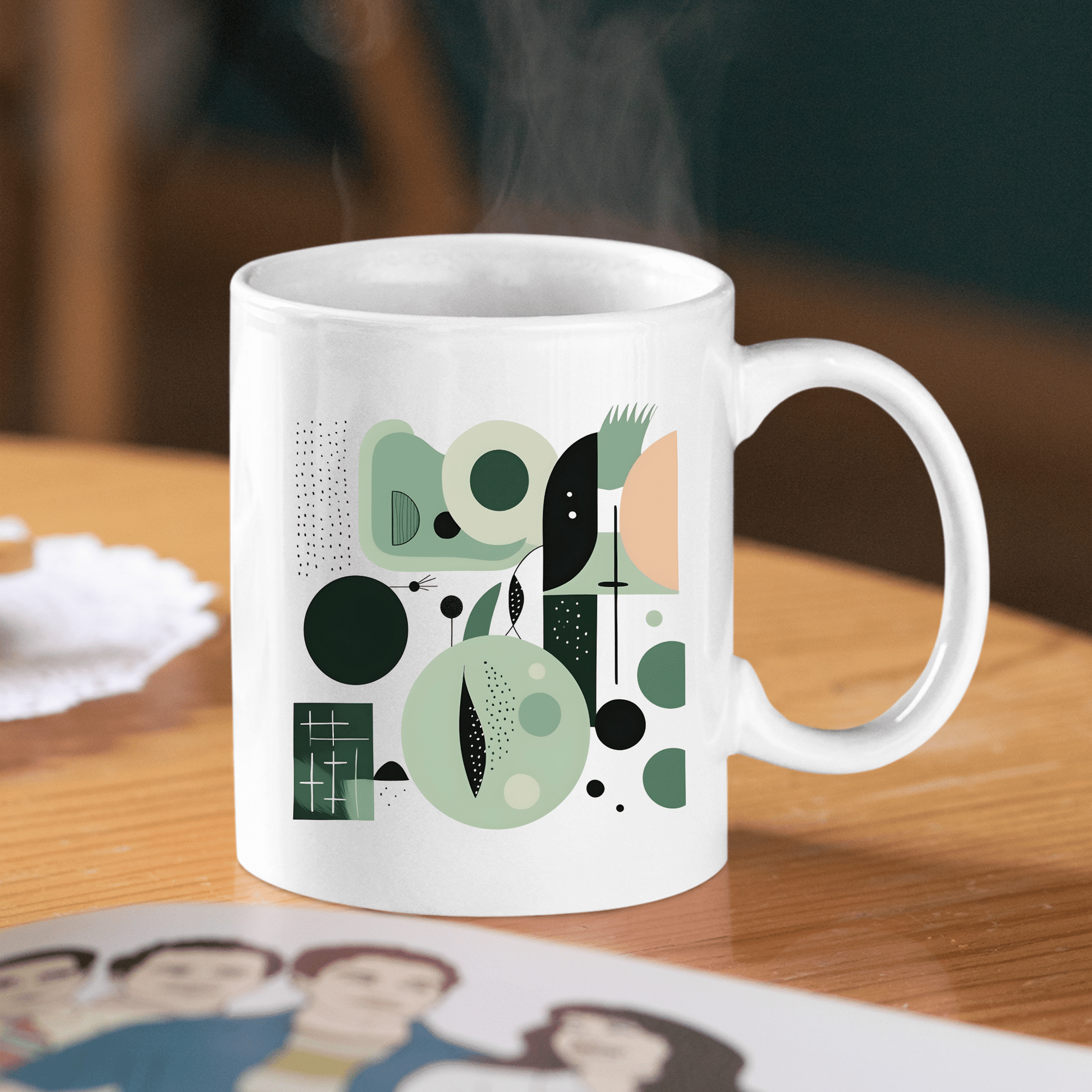 The Spring Geometry Mid Century Modern Mug, featuring a white base with abstract geometric patterns in green, black, and beige, sits on a wooden table beside a doily and a magazine as steam rises from it.