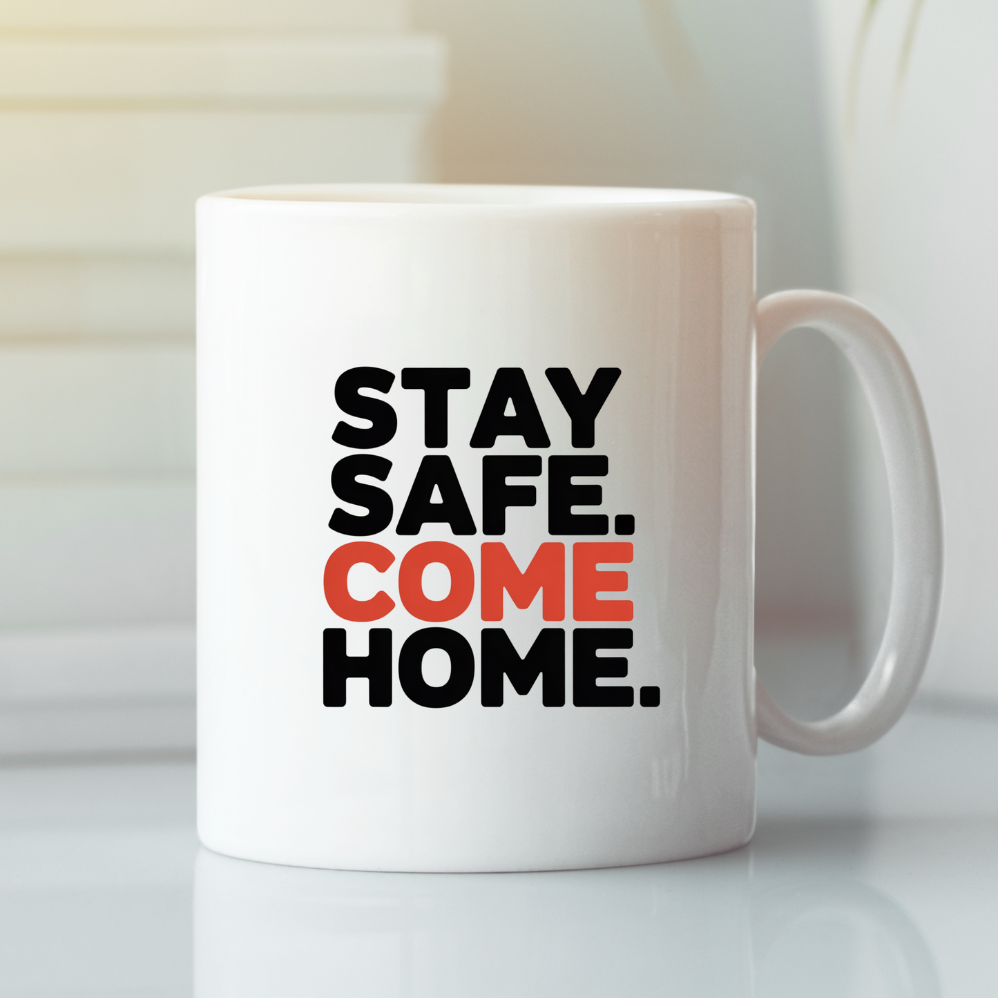 The Stay Safe Come Home Mug | Gift for First Responders features bold black and orange text that reads "STAY SAFE. COME HOME." on a white ceramic surface, shown resting on a reflective surface with a softly blurred background—making it an ideal meaningful gift for police officers or first responders.