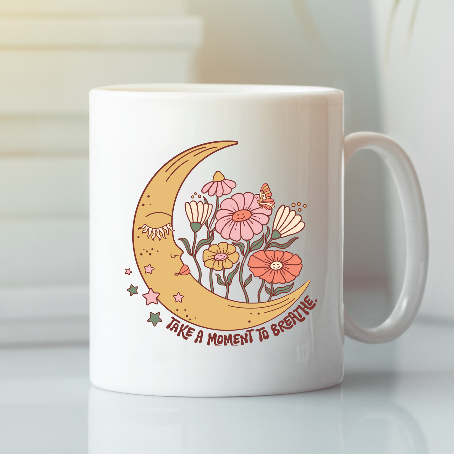The "Take a Moment to Breathe Mug | Mindfulness Coffee Mug" features an illustration of a smiling crescent moon surrounded by vibrant flowers and twinkling stars. Beneath the artwork, the phrase "Take a moment to breathe" is displayed, making this mug an uplifting choice for your coffee break or a thoughtful gift for anyone who enjoys meditation. The mug is shown resting on a reflective surface.