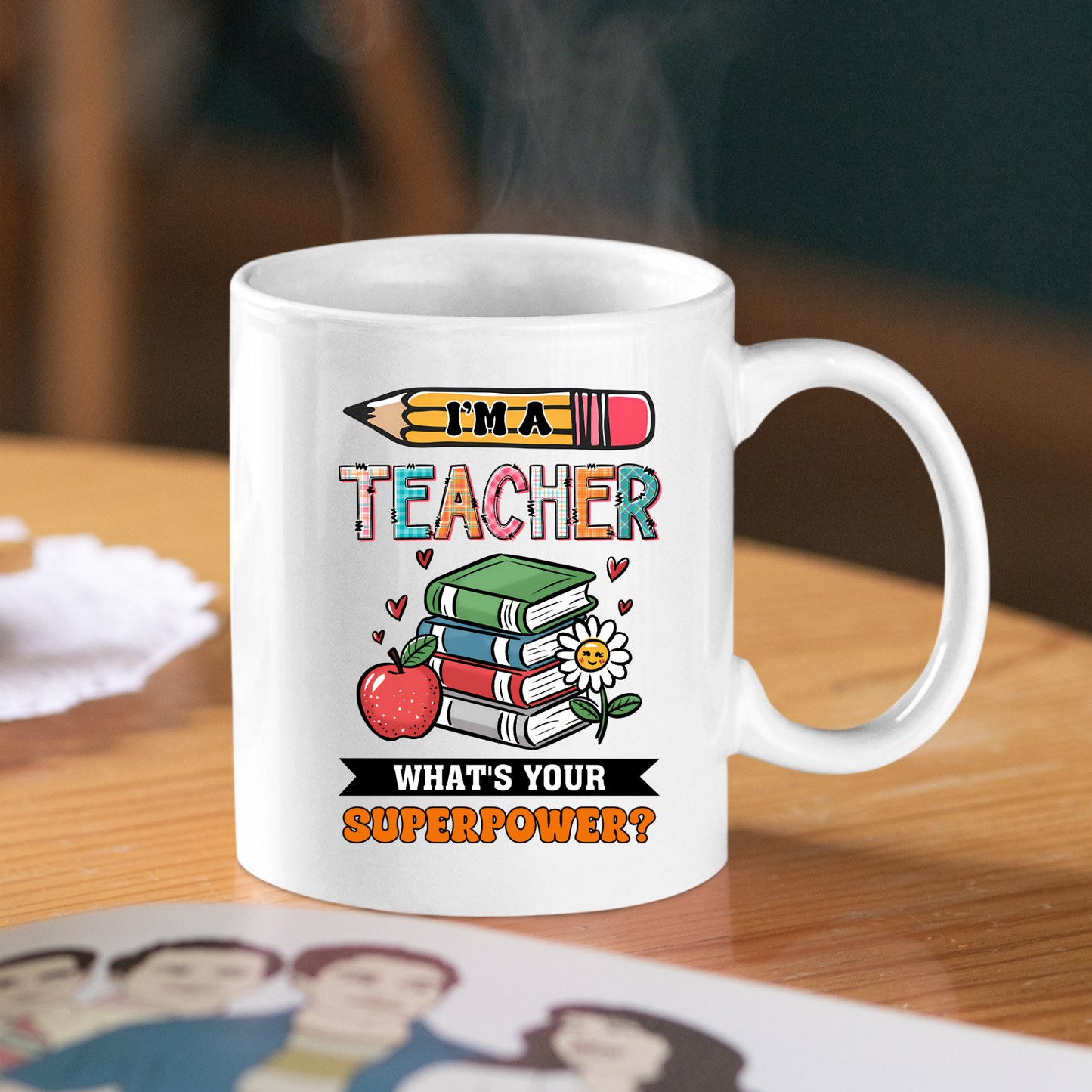 The “I’m a Teacher, What’s Your Superpower Mug” is a white ceramic mug with colorful pencil, book, apple, and flower illustrations—an ideal teacher gift. It features the fun quote on the front and sits on a wooden table beside a magazine.