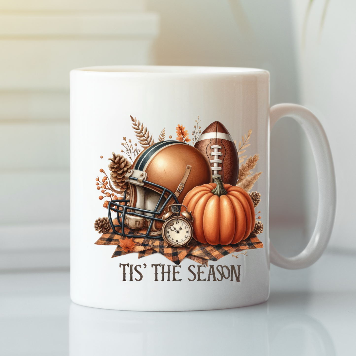 The "Tis' the Season Football Mug | Fall Pumpkins & Game Day Vibes" features a football helmet, football, pumpkins, clock, and autumn leaves on plaid with “TIS’ THE SEASON” printed underneath.