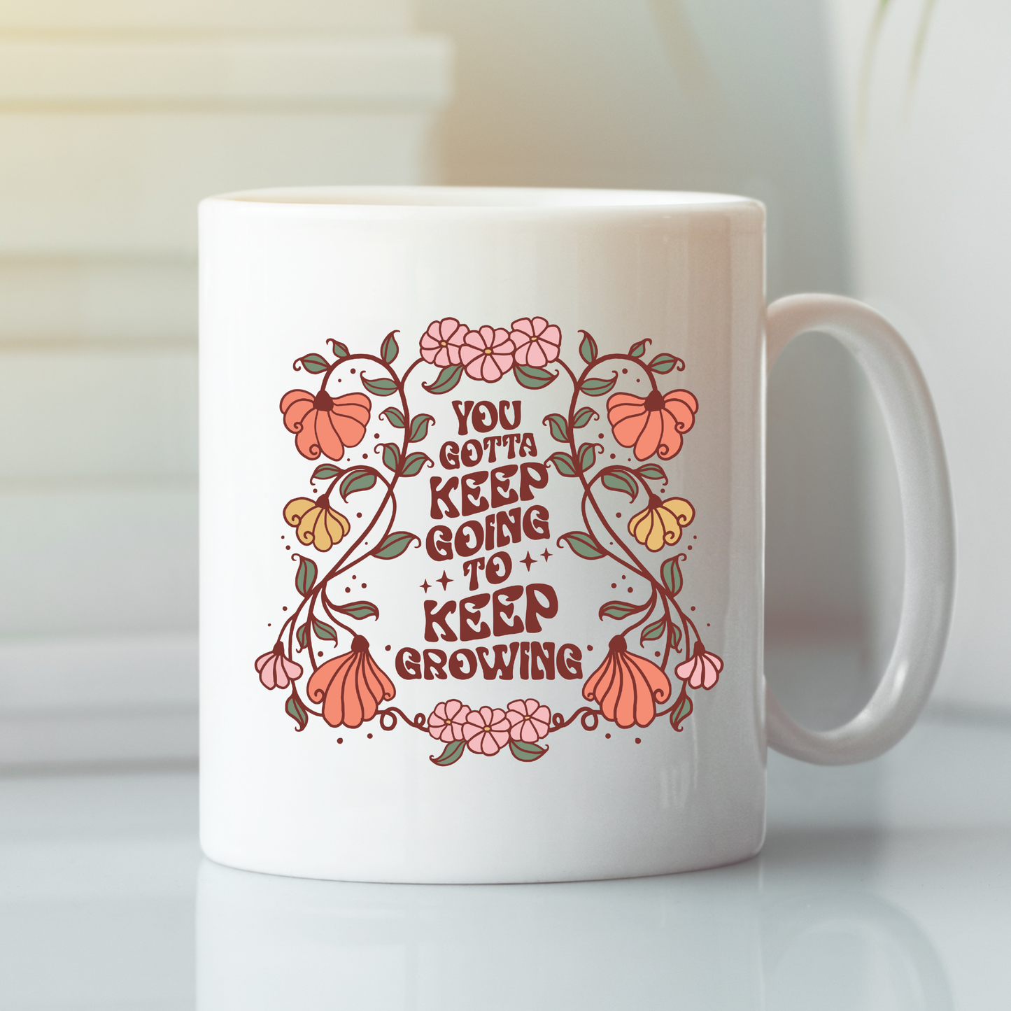 Introducing the Keep Going Keep Growing Mug | Inspirational Gift—a white ceramic mug featuring a beautiful floral design with pink and orange flowers and lush green leaves. Centered on the mug is the uplifting message, “You gotta keep going to keep growing.” Elegantly displayed on a white surface, this inspirational mug motivates you with every sip—making it the perfect gift for encouragement and daily inspiration.